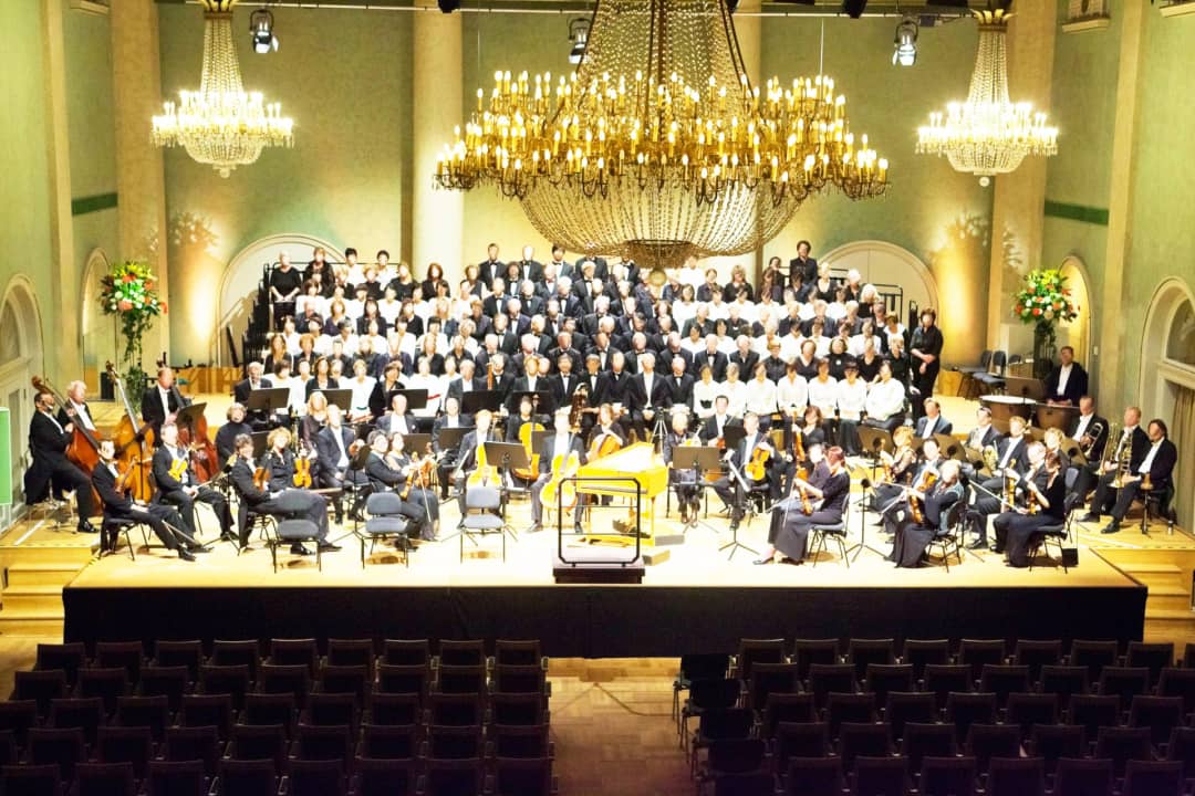 Chor und Orchester auf einer gestuften Bühne in einem Konzertsaal
