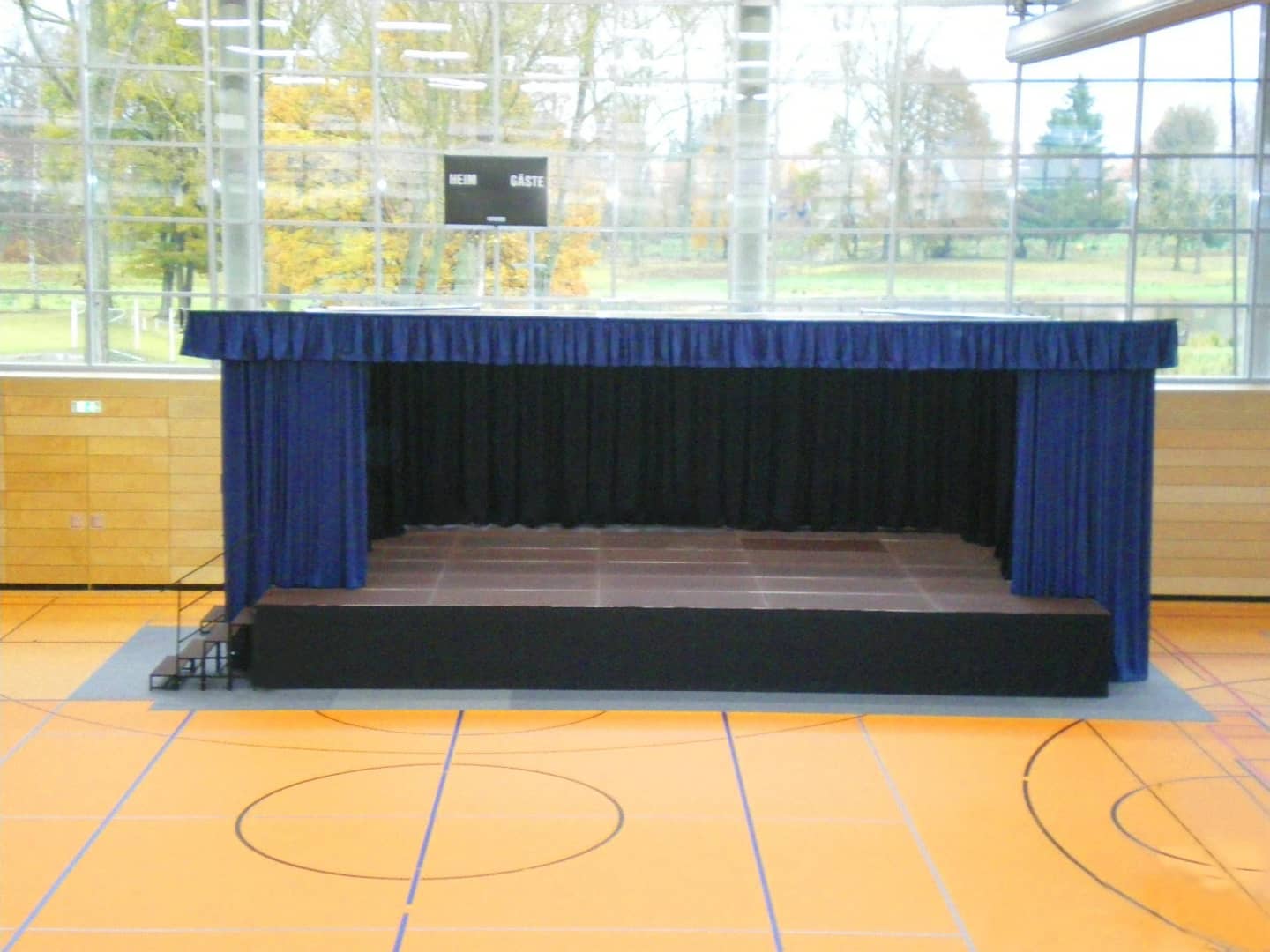Mobile stage cabinet with a blue main curtain on platforms in a sports hall