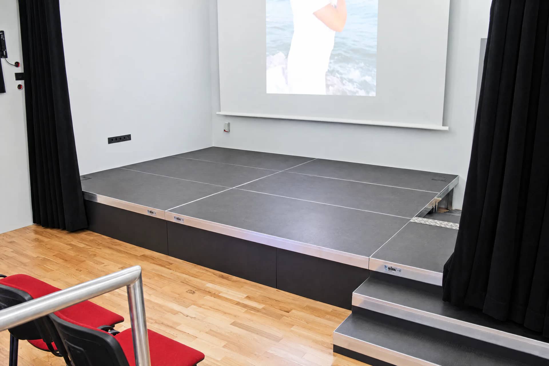 Bühne aus BÜTEC Standard-Podesten mit Aluminiumtreppe vor einer Leinwand